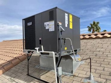 A rooftop HVAC unit installed on a residential tiled roof under a blue sky.