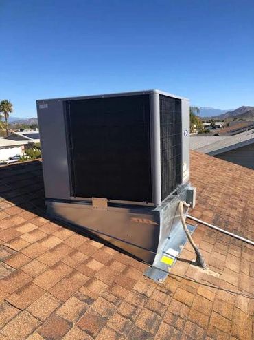 A rooftop HVAC unit installed on shingle roof under clear blue sky.