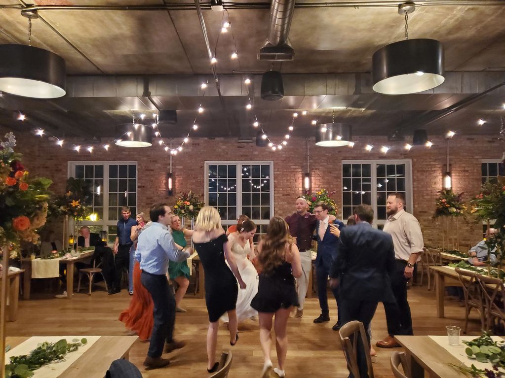 Bride Dancing to song with guests dancing with bride with bistro lights hung from the ceiling