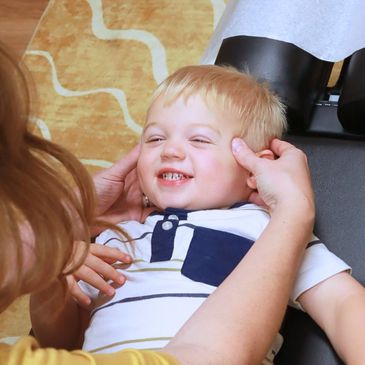 A blonde haired toddler smiling as he receives a chiropractic adjustment