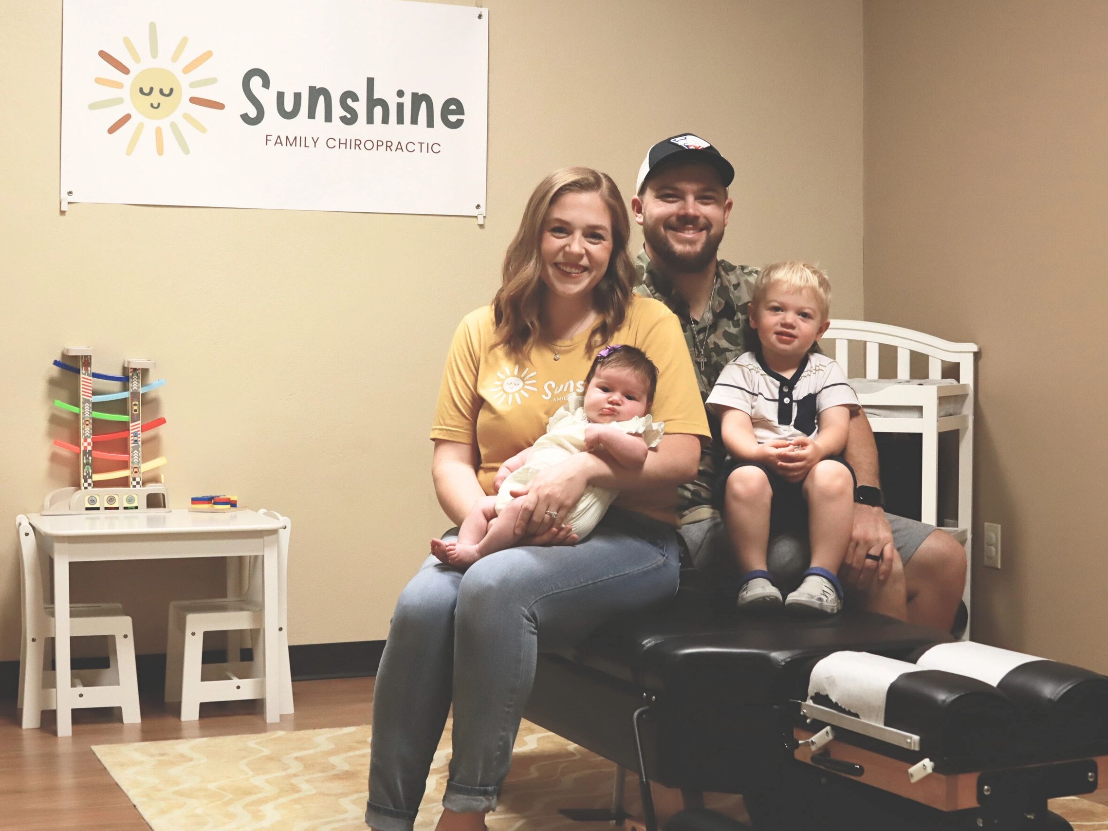 Family smiling in a chiropractors office with a sign that says "Sunshine Family Chiropractic"