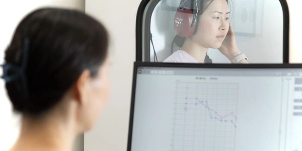 Woman undergoing a hearing test wearing headphones in a soundproof booth.