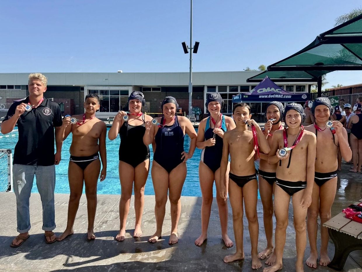Youth water polo team proudly displaying medals by the pool.