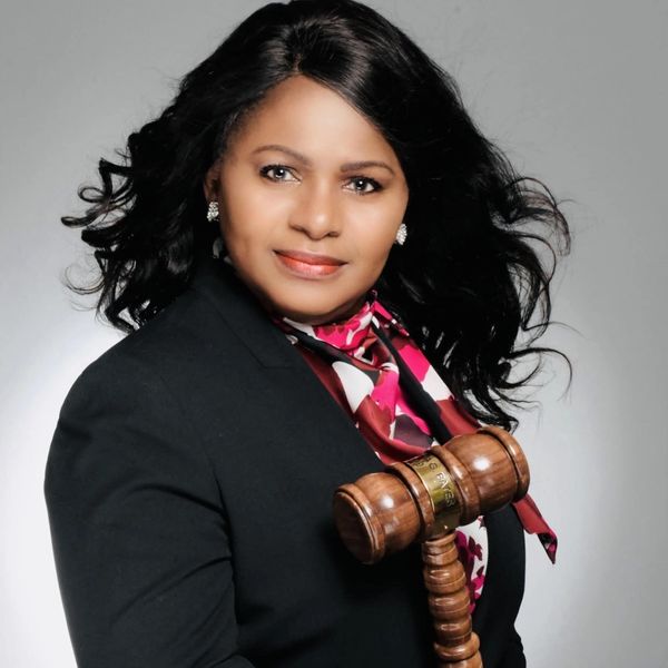 Confident woman holding a wooden judge's gavel, wearing a black blazer and floral scarf.