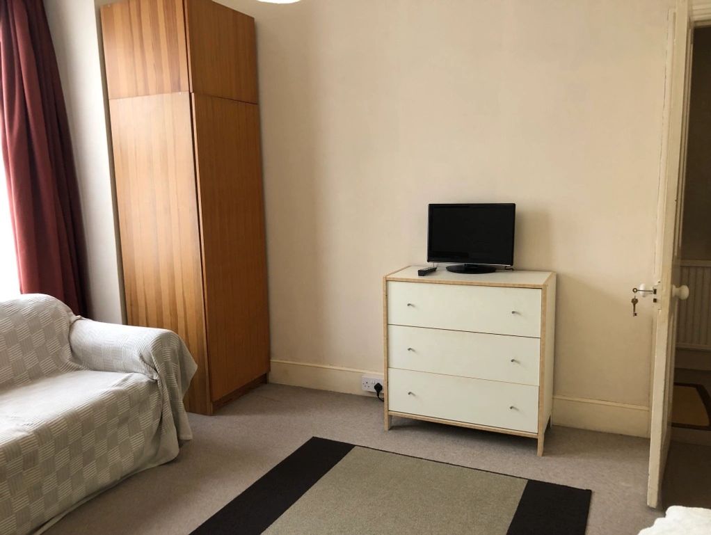 Minimalist room with a sofa, wooden wardrobe, dresser, and small TV.
