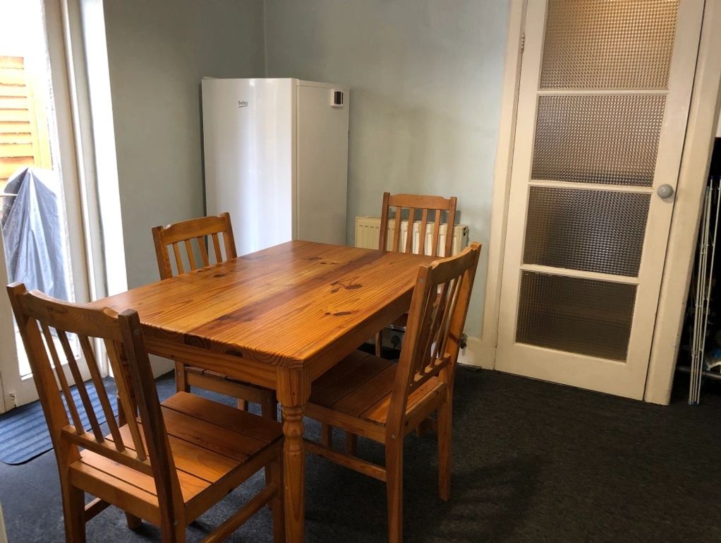Wooden dining table with four chairs in a simple kitchen corner.