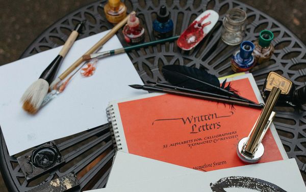 Calligraphy tools and ink on a decorative metal table with a calligraphy book.