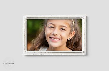 Curly haired girl smiling outside, in rustic white picture frame