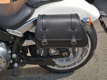 Black leather motorcycle saddlebag attached to a white bike.