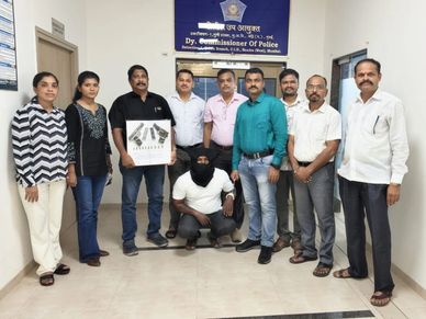Police officers pose with a black-masked detainee and seized firearms.