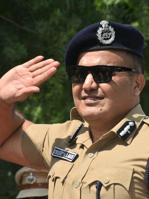 Police officer saluting outdoors in uniform and sunglasses.
