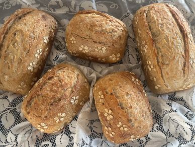 Five freshly baked oat-topped loaves of bread on a lace tablecloth.