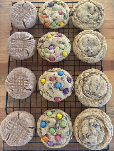 Four rows of assorted freshly baked cookies cooling on a rack.
