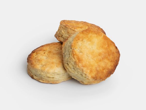 Three freshly baked flaky biscuits stacked partially atop one another with a golden-brown top.
