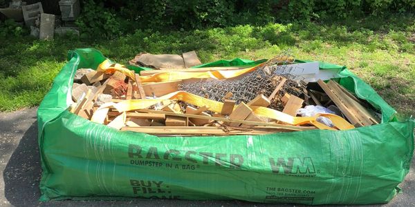 Large green dumpster bag filled with construction debris and wood pieces outdoors.