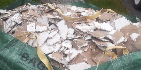 A large green bag filled with broken drywall pieces.