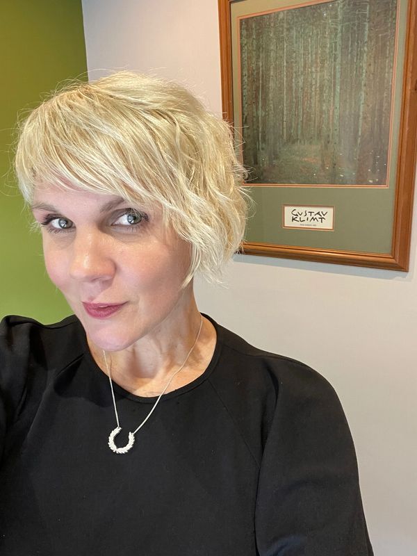 Smiling woman with short blonde hair wearing a black top and silver necklace.