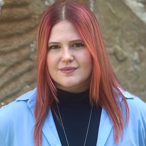 Woman with straight reddish hair and blue coat.