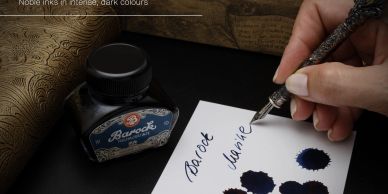 Hand writes with a fountain pen using dark blue ink on paper next to an ink bottle.