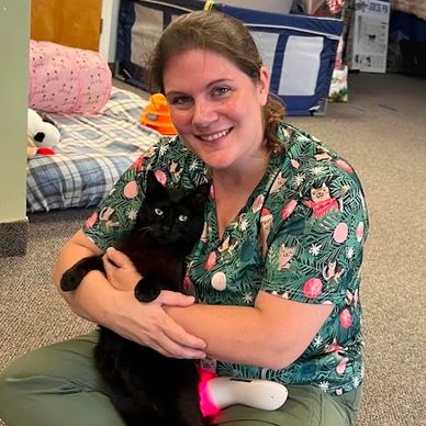Woman smiling and holding a black cat indoors.