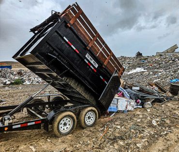 A trailer unloading garbage at a landfill site on a cloudy day.