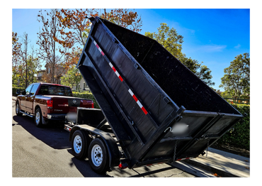 A red Nissan Titan towing a black dump trailer raised at an angle.