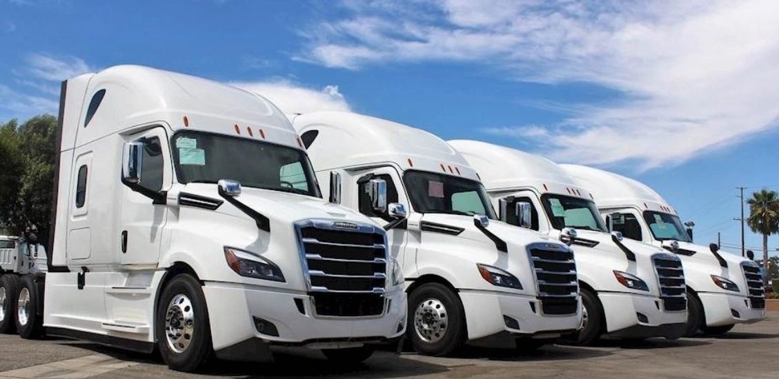 A row of four white semi trucks parked under a blue sky.