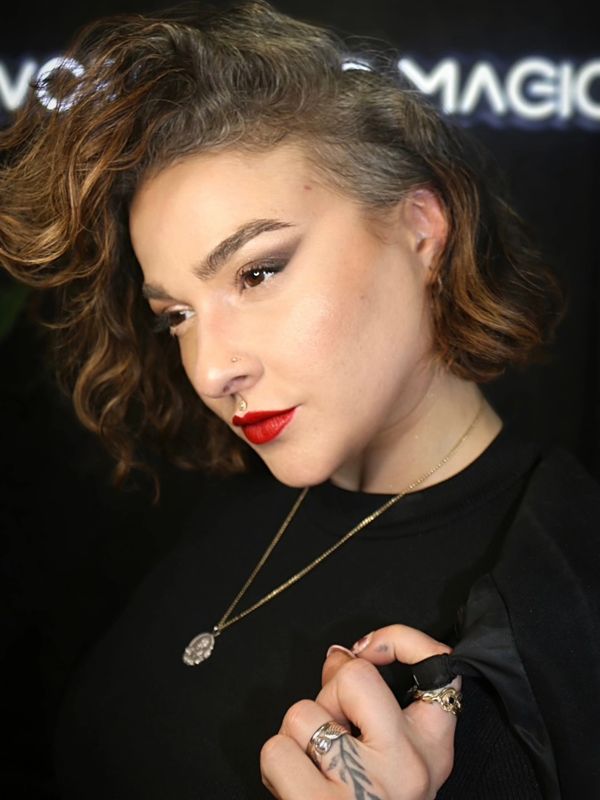 Young woman in front of a neon sign wearing red lipstick and gold jewelry.