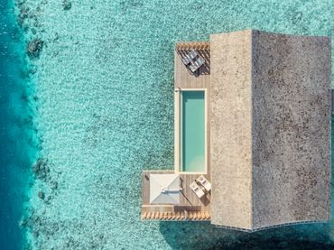 Aerial view of a villa with a pool surrounded by clear turquoise water.
