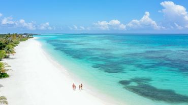 A family walks along a pristine white sandy beach beside clear turquoise waters.