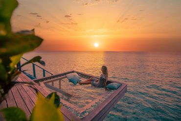 Woman relaxing on a net hammock overlooking the ocean at sunset.