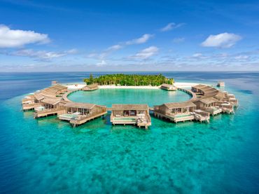 Overwater bungalows arranged in a circle around a tropical island lagoon.