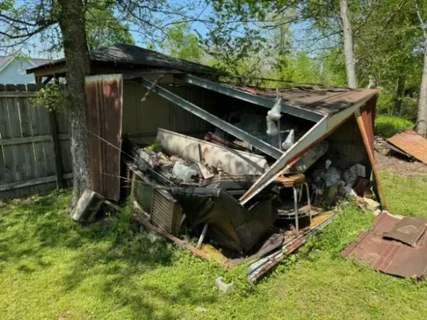 Collapsed rusty metal shed in a green backyard with scattered debris.