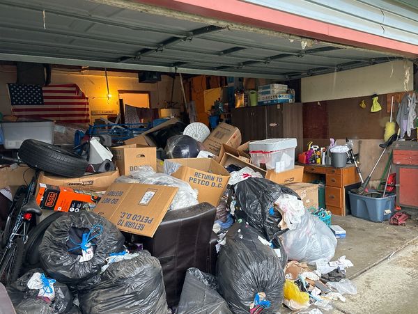 Cluttered garage filled with boxes, bags, and miscellaneous items.