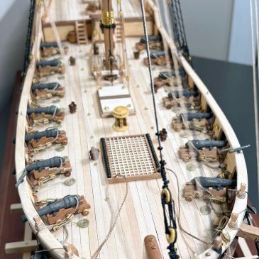 Detailed model ship deck with cannons and rigging.
