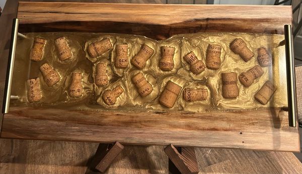 Wooden serving tray with embedded wine corks in resin and brass handles.
