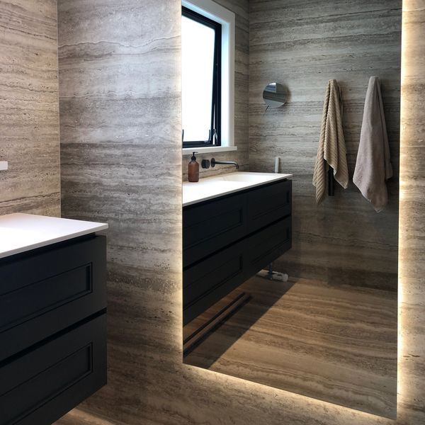 Modern bathroom with large illuminated mirror and dark cabinetry.