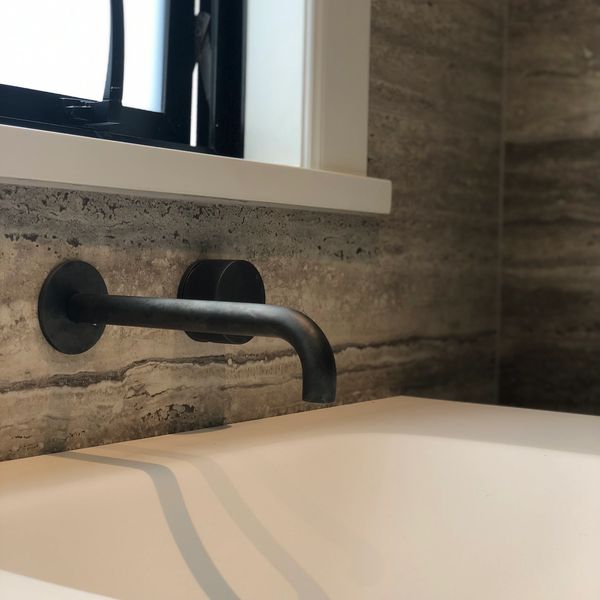 Minimalist bathroom sink with wall-mounted black faucet and stone backsplash.