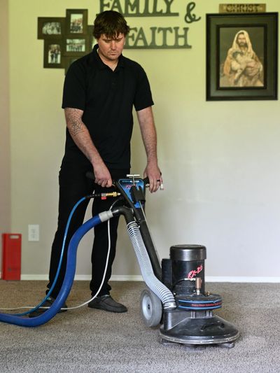 Man cleaning carpet with a professional machine in a living room.