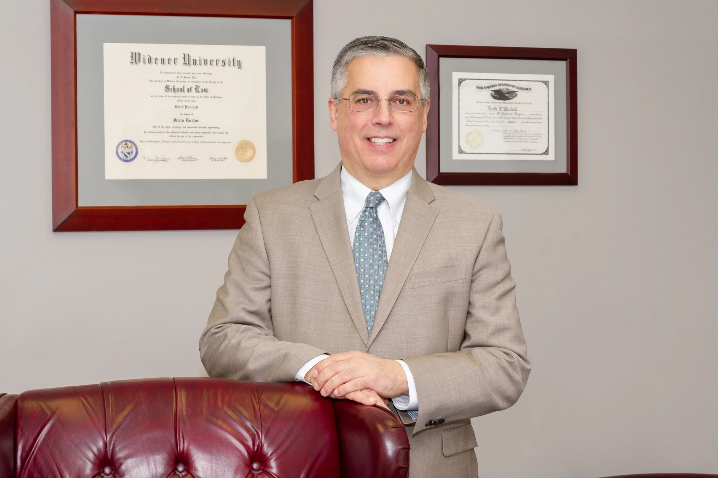 Attorney Pavlack posing for a photo in his office with his diplomas hanging on the wall behind him a
