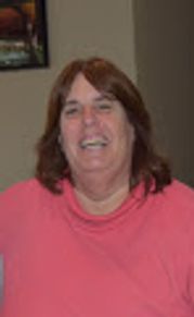 A smiling woman with brown hair wearing a pink top.