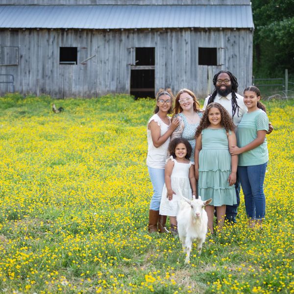 Happy family posing in a yellow flower field with a white goat in front.