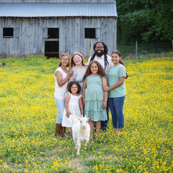 Happy family posing in a yellow flower field with a white goat in front.