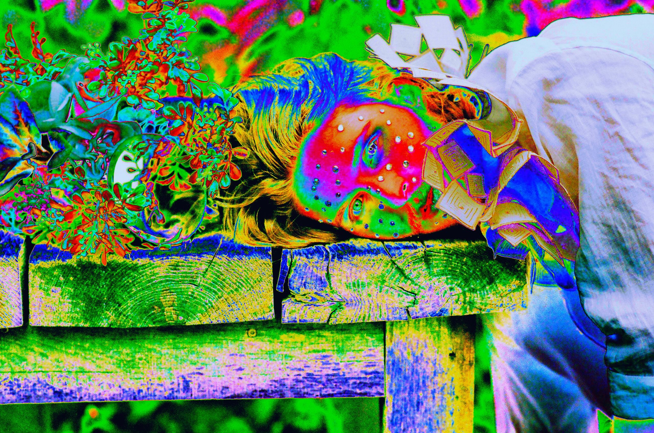 A man places his head onto a table filled with flowers. This image is in hypercolor.