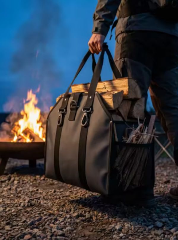 Woodsman log bag being carried beside an outdoor fire pit, filled with logs and designed for practic