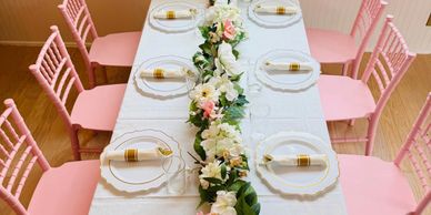 Elegant table setup with pink chairs and floral centerpiece.