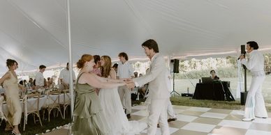 People dancing joyfully under a white tent at an outdoor event.