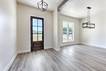 Bright empty room with wooden door, large window, and modern lighting fixtures.
