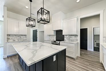 Modern kitchen with white cabinetry, marble countertops, and black pendant lighting.