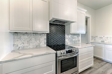 Modern kitchen with white cabinetry and a sleek black hexagonal tile backsplash behind the stove.